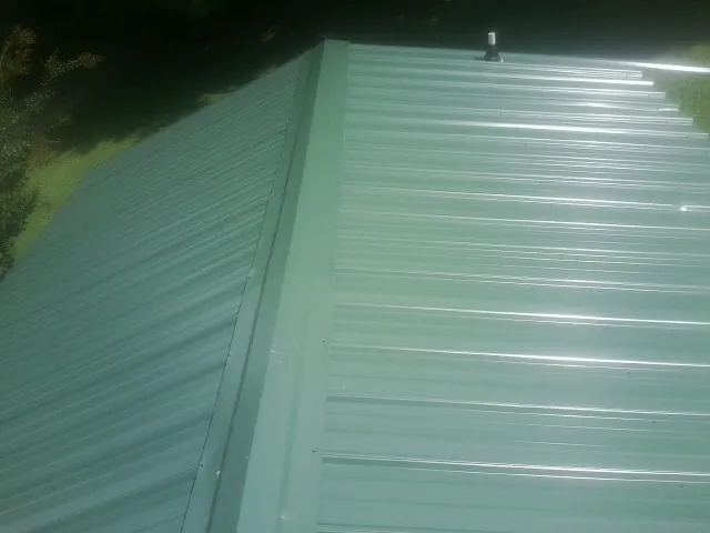 New green metal panels meeting at the ridge of a roof — Flat Roof Repair work by our crew in Twin Lakes